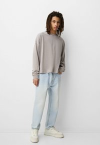 Lys grå langærmet skjorte med dropped shoulders, parret med falmede lyseblå jeans og cremede sneakers med teksturerede detaljer.