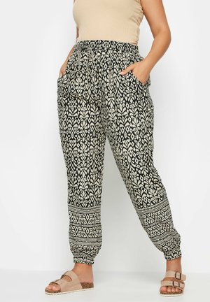 Zwarte en beige joggingbroek met een patroon, voorzien van een elastische tailleband, zijzakken en taps toelopende boorden met een geometrisch printdesign.