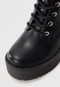 Μαύρη δερμάτινη μπότες αστράγαλου με στρογγυλή μύτη, κορδόνια μπροστά, ασημένιες μεταλλικές θηλιές και παχύ μαύρο πέλμα με υφή.