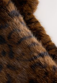 Konstpäls i bruna nyanser med svarta leopardliknande fläckar. Texturen verkar mjuk och fluffig med en naturlig, mönstrad design.