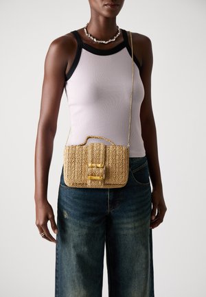 Woven straw crossbody bag, rectangular shape, gold hardware accents, and a top handle. Worn with a fitted pink tank top and denim shorts.