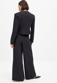 Melnas piegriezuma žaketes ar garām piedurknēm un īsu griezumu, kombinētas ar platām biksēm, abas izgatavotas no gludas auduma. Minimālisma stils, bez rakstiem.