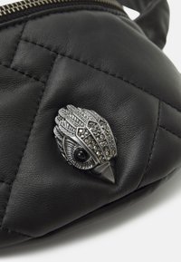 Musta tikattu nahkalaukku, jossa on metallinen lintukoriste jalokivikoristein ja sileä pinta. Yläosassa vetoketjullinen suljenta.