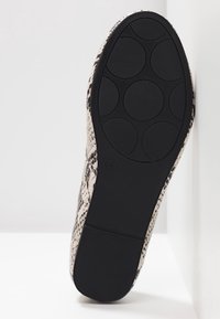 Semelle d'une chaussure plate à motif serpent avec une semelle en caoutchouc noir comportant des coussinets circulaires antidérapants et un talon texturé.