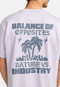 Lys lilla bomulds t-shirt med et grafisk design af palmer, byens skyline og tekst, alt sammen i mørkeblå.