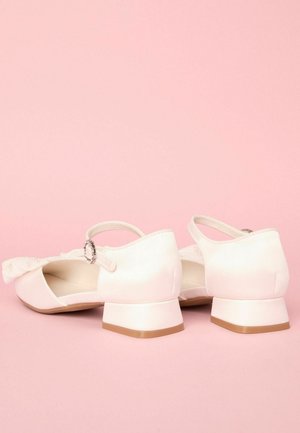 Chaussures en satin rose clair avec un détail nœud, petit talon et bride de cheville avec une boucle en argent décorative ; texture lisse et design à bout rond.