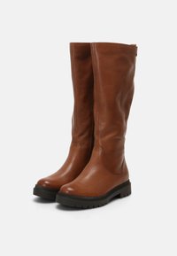 Bottes en cuir marron jusqu'au genou avec une finition texturée, une semelle robuste et un design minimaliste. Remarquables par leur tige lisse et leur bout rond.