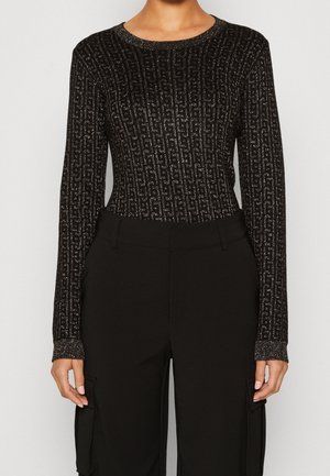 Haut en maille noir à manches longues avec motif géométrique argenté métallisé, associé à un pantalon cargo noir taille haute porté par une personne debout.