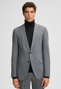 Grauer, maßgeschneiderter Blazer mit unauffälligem Karomuster, Ein-Knopf-Verschluss und Kerbkragen. Trägt man über einem schwarzen Rollkragenpullover.