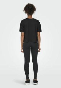 Camiseta negra corta con cuello redondo, combinada con leggings negros y zapatillas deportivas. Tejido suave, corte relajado y mangas cortas.