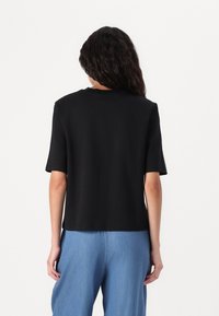 Haut noir à manches courtes en tissu lisse, avec un col rond et une coupe décontractée. Présenté avec un pantalon en denim bleu clair.