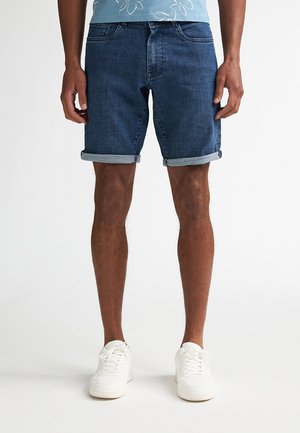 Donkere blauwe denimshorts met omgeslagen zoom, voorzien van vijf zakken en een ritssluiting. Draag ze met witte sneakers voor een contrast.
