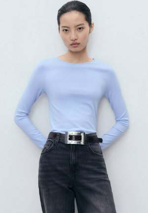 Top azzurro chiaro a maniche lunghe con scollatura rotonda, abbinato a jeans neri a vita alta e una cintura larga con fibbia argentata. Texture liscia.