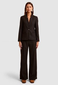 Black pinstripe suit featuring a fitted blazer with a single button closure and wide-legged trousers. Smooth fabric texture.