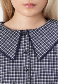 Abito a righe blu navy e bianche con un ampio colletto, dotato di chiusura a bottoni e rifinitura in pizzo lungo i bordi del colletto. Il tessuto ha una trama testurizzata.