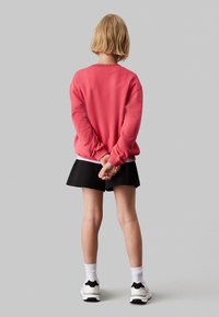 Felpa rosa con polsini e fondo a coste, abbinata a una gonna nera. Calze bianche e sneakers completano il look. Vista posteriore mostrata.