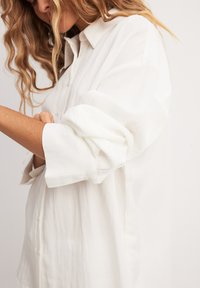 Witte button-up blouse gemaakt van lichtgewicht stof, met een klassieke kraag, opgerolde mouwen en een losse pasvorm zonder zichtbare patronen.