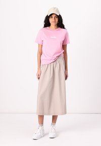 Lyserød bomulds t-shirt med frontlogo, parret med en beige høj talje maxi nederdel. Hvide sneakers fuldender outfittet.