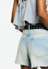 Ljusblå denimshorts med fransad sidsöm, två bakfickor och ett svart nitarbälte. Toppen är en lös, randig klädnad med knytningar.