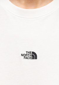 Λευκό βαμβακερό t-shirt με μικρό μαύρο κεντημένο λογότυπο με καμπύλες γραμμές, που γράφει "THE NORTH FACE" στην αριστερή πλευρά του στή θους.