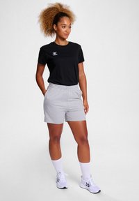 Black cotton t-shirt with white logo, paired with gray cotton shorts. Model wears white athletic shoes and knee-high white socks.