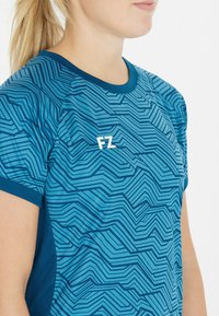 Kortærmet atletisk skjorte i lyseblå med mørkeblåt zigzag-mønster, med rund halsudskæring og hvidt logo "FZ" på brystet.