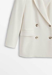 Blazer croisé blanc cassé avec quatre boutons métalliques, revers cranté, manches longues et une poche à rabat sur le côté gauche.