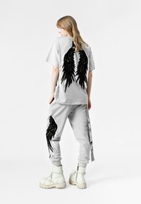 Camiseta gris de gran tamaño con diseño de alas negras en la parte posterior; pantalones jogger gris a juego con detalles de alas negras, combinados con botas gruesas blancas.