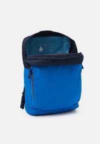 Blue backpack with a zippered opening, featuring a navy top flap and interior pocket with a name tag. Made from durable fabric with a smooth texture.