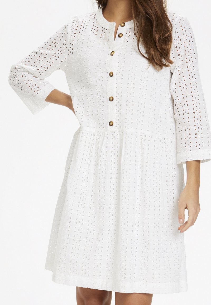 Weißes Kleid mit Lochmuster, Dreiviertelärmeln, runder Ausschnitt und bronzefarbenem Knopfverschluss vorne. A-Linie Silhouette.