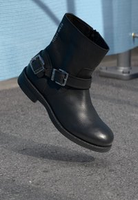 Svart lær ankelstøvel med teksturfinish, sølvspenner og lav hæl. Støvelen har glidelås på siden for enkel påkledning.