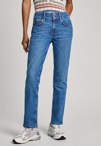 Ljust blå denimjeans med rak skärning, som har en dubbel knappstängning, fyra fickor och subtil blekning. I kombination med grå sneakers.