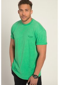 Camiseta de algodón verde con cuello redondo, mangas cortas y una textura desteñida. Presenta un pequeño texto negro en el lado izquierdo del pecho.