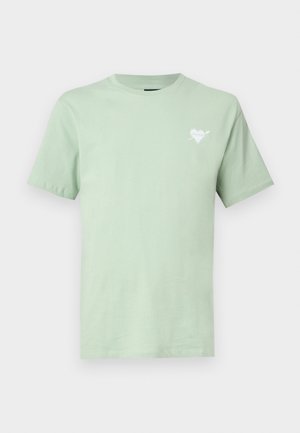 T-shirt vert clair à col rond avec manches courtes et petit logo blanc en forme de cœur avec une flèche sur le côté gauche de la poitrine.