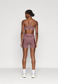 Μωβ αθλητικό σουτιέν με ρυθμιζόμενες τιράντες και λεπτομέρεια λογότυπου, σετ με ταιριαστά σορτς που διαθέτουν ψηλή μέση και πλαϊνές διχτυωτές λεπτομέρειες.