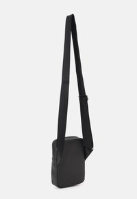 Sort crossbody taske lavet af glat syntetisk materiale, med rektangulær form, justerbar rem og lynlås.