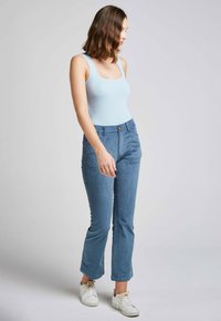 Débardeur côtelé bleu clair associé à un pantalon en velours côtelé bleu clair, avec une fermeture à boutons et deux poches avant. Des baskets blanches complètent le look.