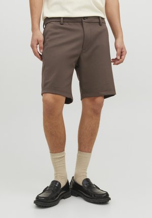 Shorts marron avec une texture lisse, une coupe décontractée, un ourlet retourné et des poches latérales, associés à des chaussettes beiges et des mocassins noirs.