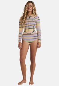 T-shirt a maniche lunghe, a righe multicolori, con cappuccio e zip frontale; presenta una patch con logo sul petto. Il materiale è elastico e aderente.