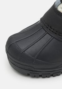 Bota negra impermeable con un exterior de goma texturizada, que presenta un detalle acanalado en la puntera y una suela robusta y con patrón para mayor tracción.