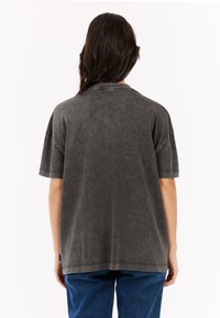 Oversized grijze katoenen shirt met een getextureerde afwerking, korte mouwen en een ronde halslijn. Bevat zichtbare stiksels en heeft een ontspannen pasvorm.