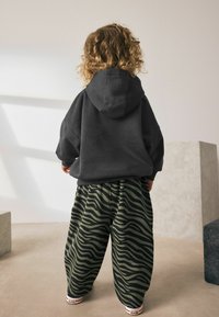 Dark gray hoodie with a large hood, paired with loose-fitting green pants featuring a black zebra stripe pattern. White sneakers are visible.