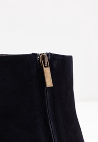 Marineblauwe suède enkellaars met een zijrits en een metalen treklipje. Het ontwerp is slank met een zachte textuur en een gestructureerde vorm.