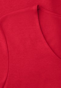 Gros plan d'un tissu rouge avec des coutures visibles et des plis superposés, montrant la texture et les détails des coutures.