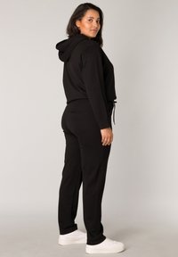 Zwarte hoodie jumpsuit met een tailleband met trekkoorden, lange mouwen en zijzakken. Gladde stof en een getailleerd ontwerp met een hedendaagse silhouet.