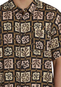 Camisa de manga corta con un fondo negro y un patrón repetitivo de flores y hojas en tonos beige, rosa y marrón. Diseño de apertura con botones.