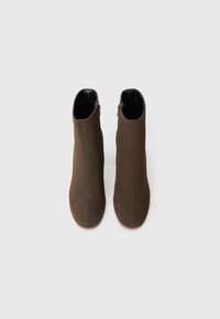Bottines brunes avec une texture en suede lisse, dotées d'une fermeture éclair latérale et d'un design minimaliste. Pointe arrondie et semelle plate.
