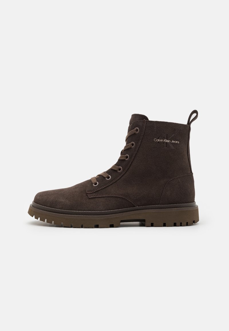 Stivale alla caviglia in suede marrone scuro con lacci, suola robusta e logo Calvin Klein Jeans sul lato, mostrato in vista profilo su sfondo bianco.