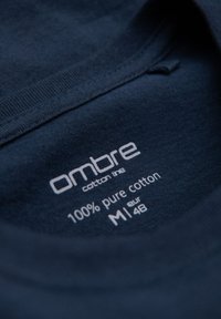 Mørkeblå bomuldsskjortelabel med mærket "ombre," 100 % ren bomuld, størrelse M (EUR 48) inde i halsudskæringen.