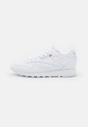 Bílé tenisky Reebok s hladkým syntetickým svrškem, šněrováním, polstrovaným límcem a zdrsněnou gumovou podrážkou se subtilním logem.